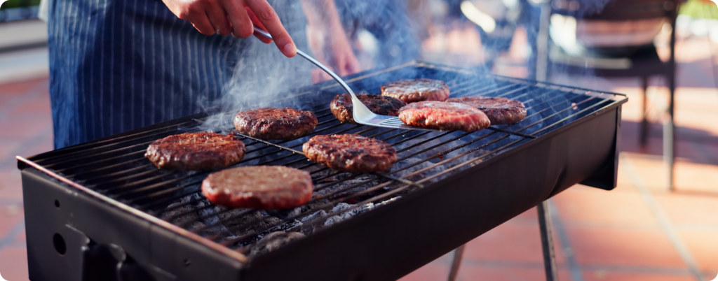 A man cooking burger patties in the backyard